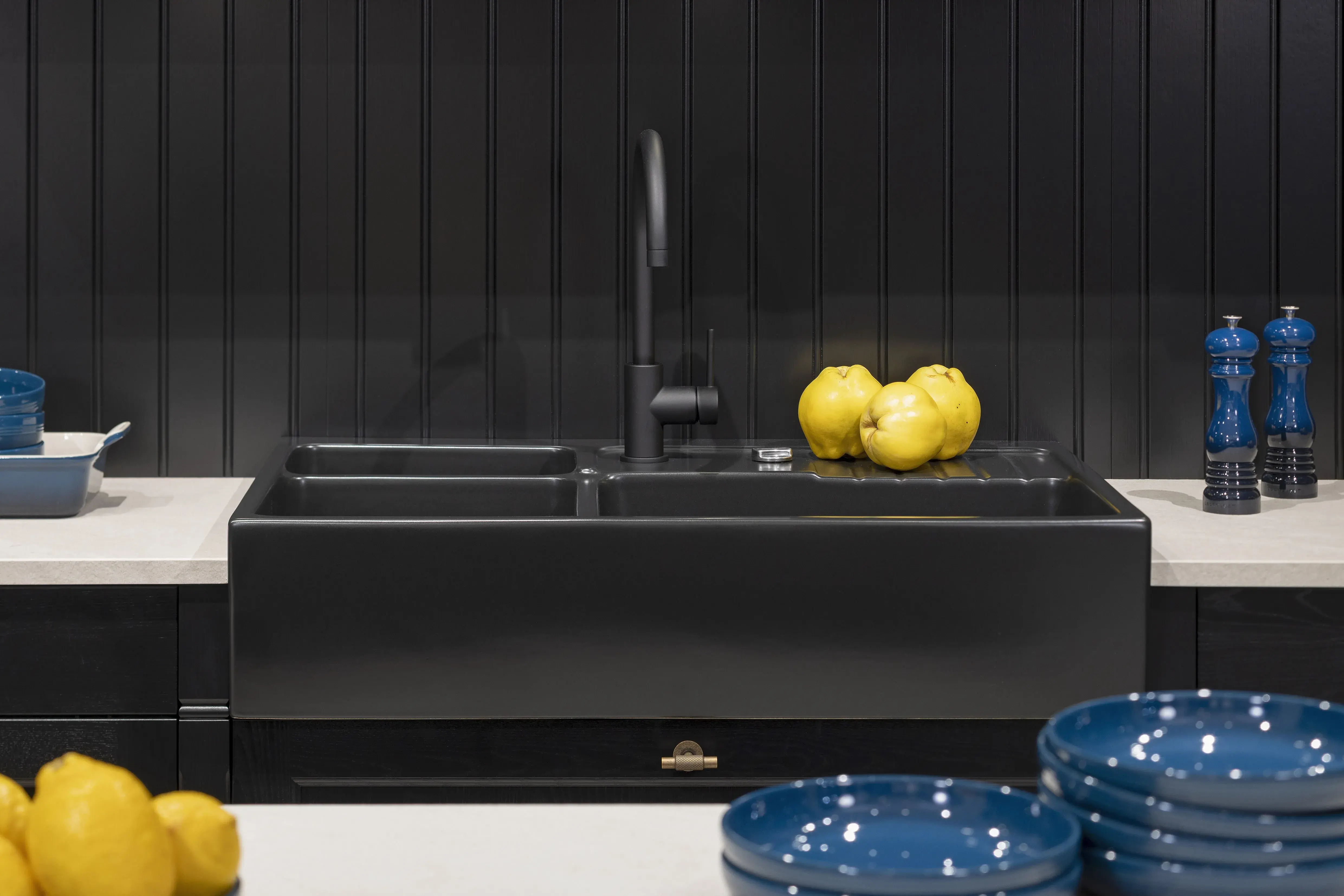 Schwarze Küchenspüle, gelbe Zitronen, blaue Schüsseln und Salz- und Pfeffermühlen.