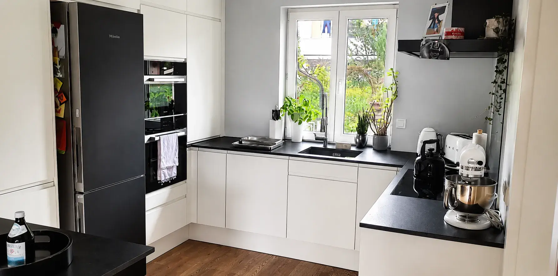 Hochwertige Designküche mit weißen grifflosen Fronten, schwarzer Arbeitsplatte, integriertem Backofen, Kühl-Gefrierkombination und modernem Spülbereich.