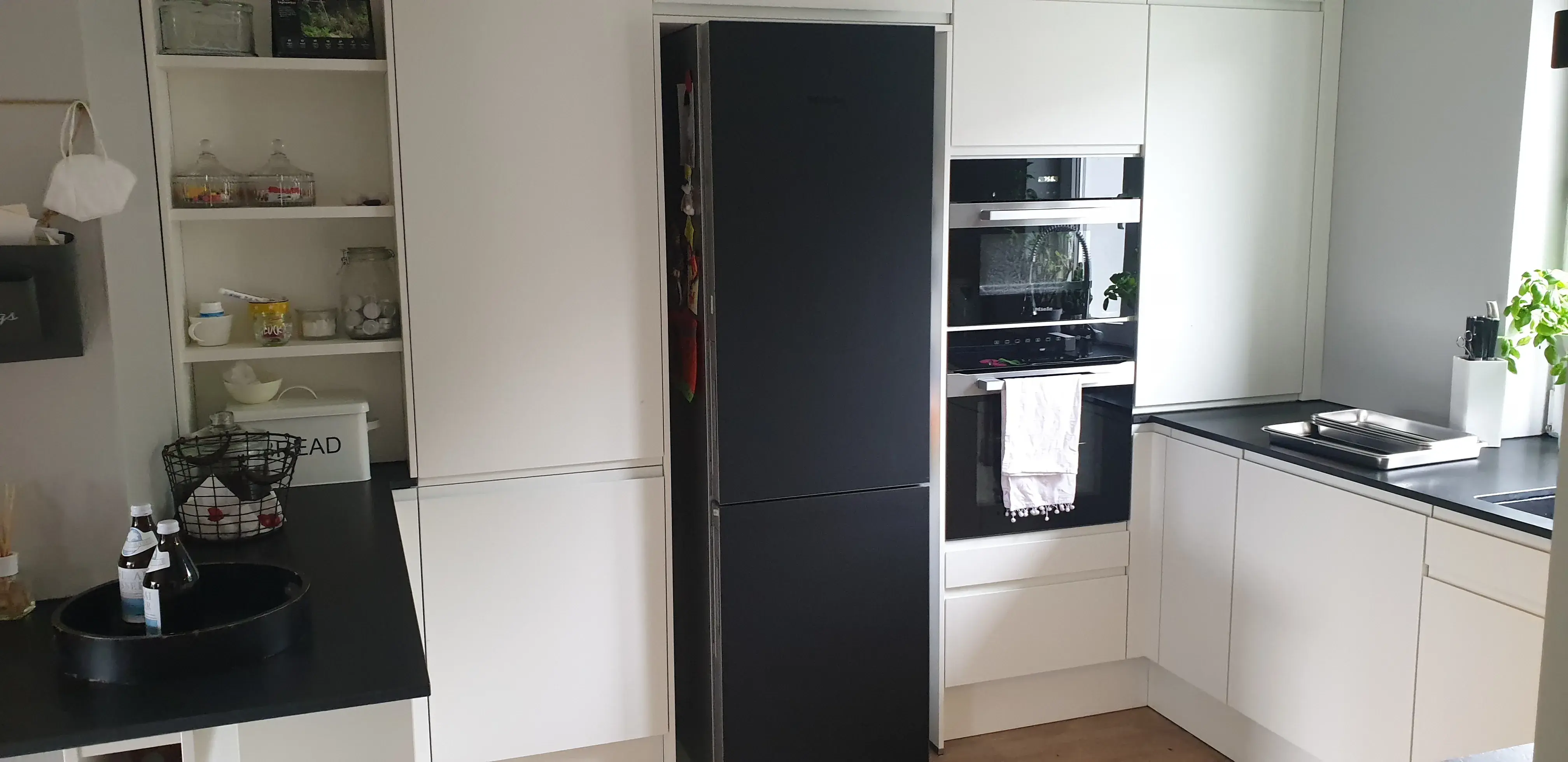 Moderne weiße Einbauküche nach Maß mit grifflosen Fronten, schwarzer Arbeitsplatte, Miele-Einbaugeräten und viel Stauraum.