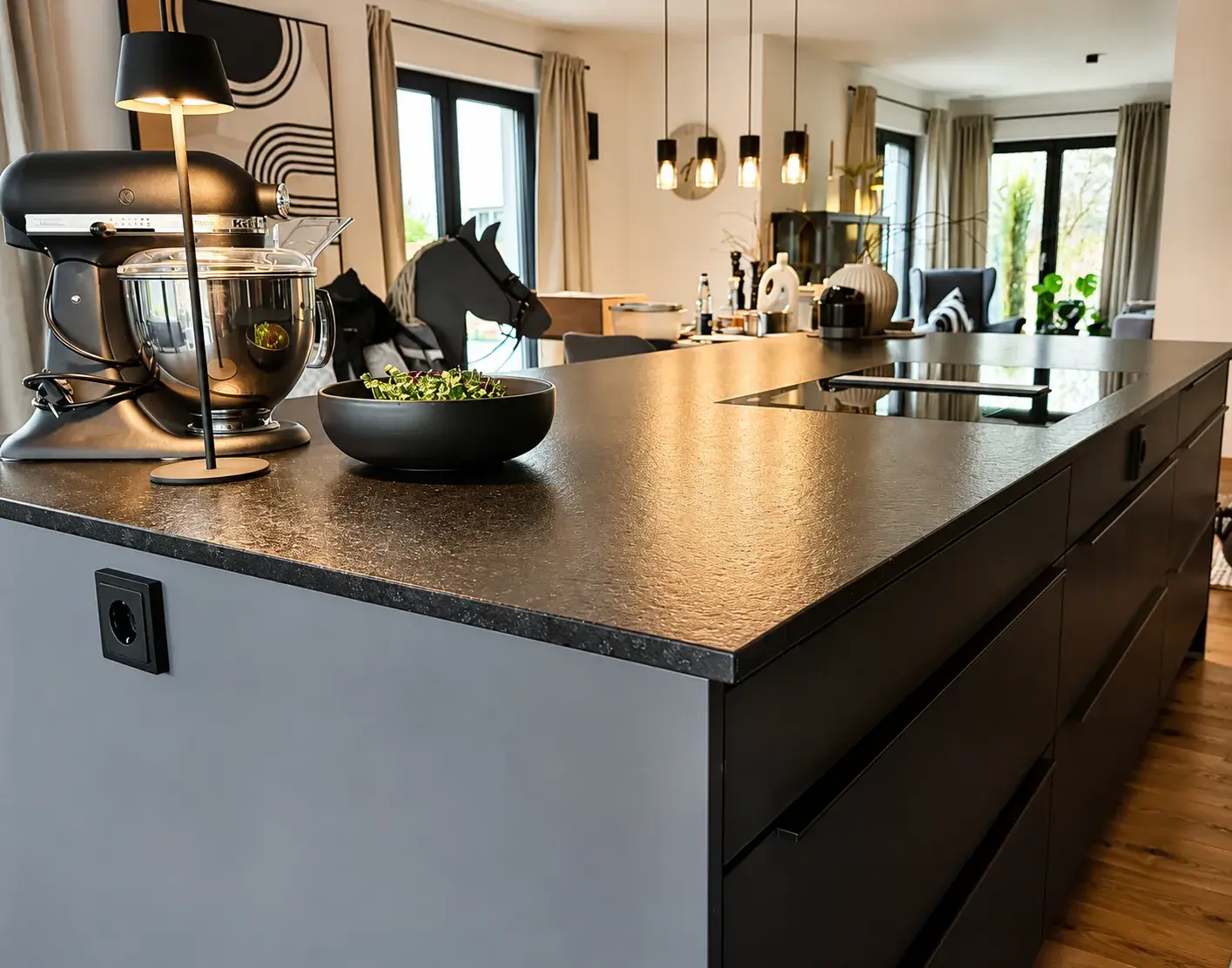 Moderne Designküche mit schwarzer Kochinsel, flächenbündigem Kochfeld, hochwertiger Arbeitsplatte und offenem Wohn- und Essbereich.