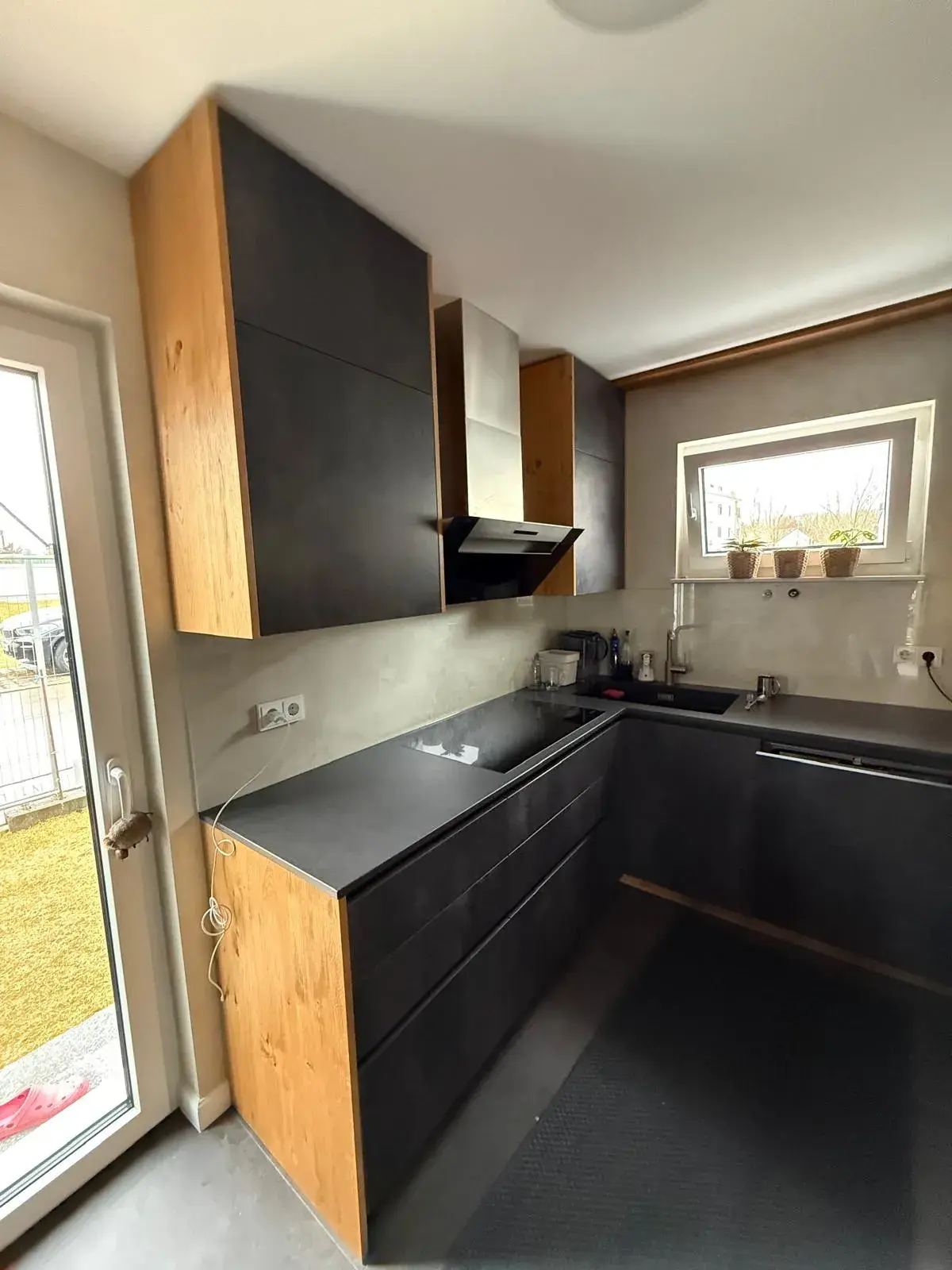 Hochwertige Designküche mit anthrazitfarbenen Fronten in Betonoptik, Eichenholzoptik, grifflosen Schränken, Induktionskochfeld und modernem Dunstabzug.