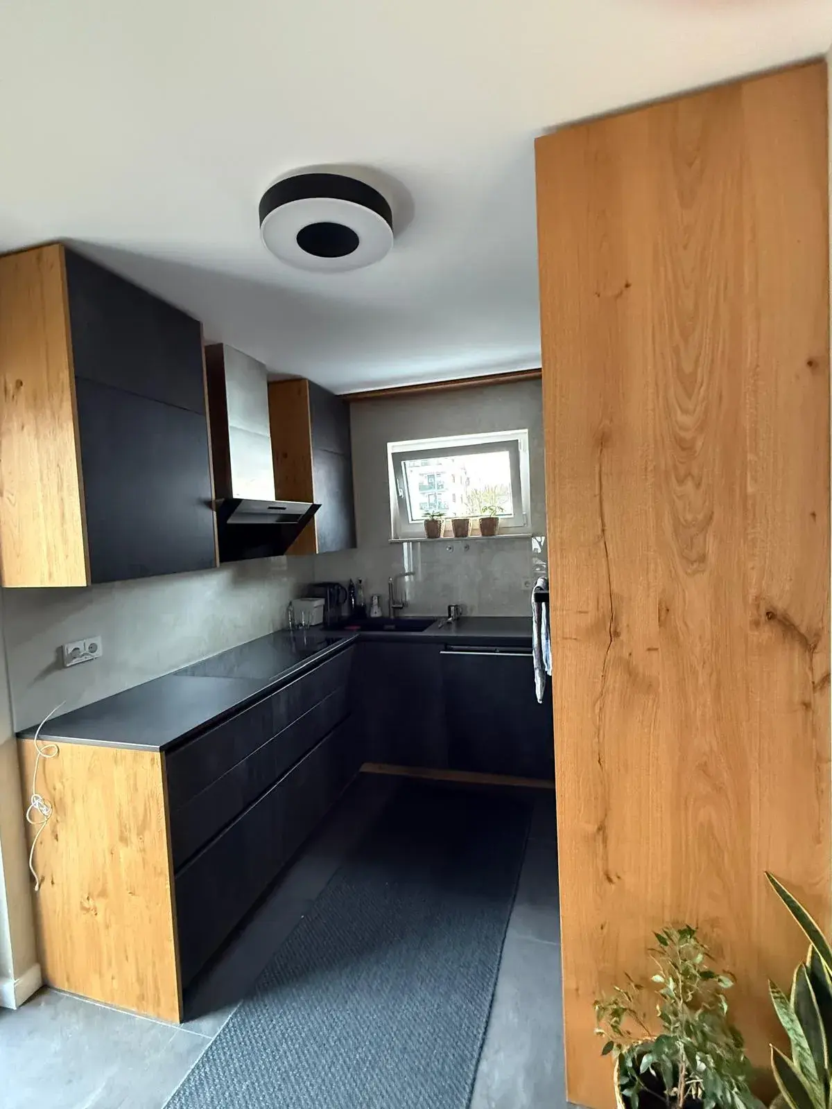 Hochwertige Designküche mit anthrazitfarbenen Fronten in Betonoptik, Eichenholz, grifflosen Schränken, Dunstabzug und moderner Küchenplanung.
