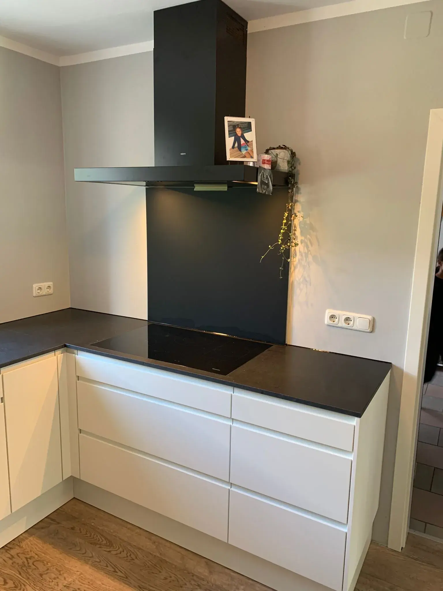 Moderne grifflos geplante Einbauküche mit weißen Fronten, schwarzer Arbeitsplatte, Induktionskochfeld und eleganter Deckenhaube in Schwarz.